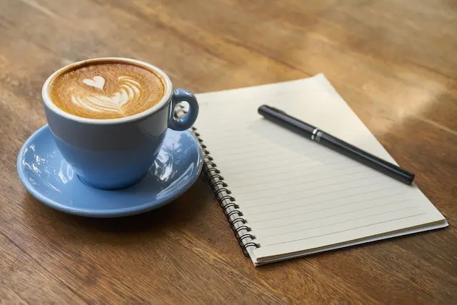 coffee on desk with notebook and pen