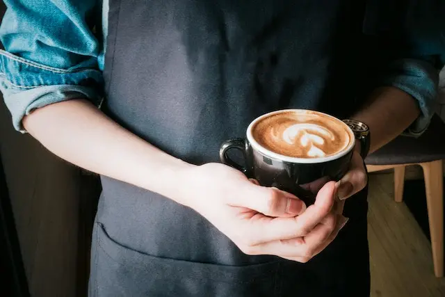 Barista in apron holding hot coffee